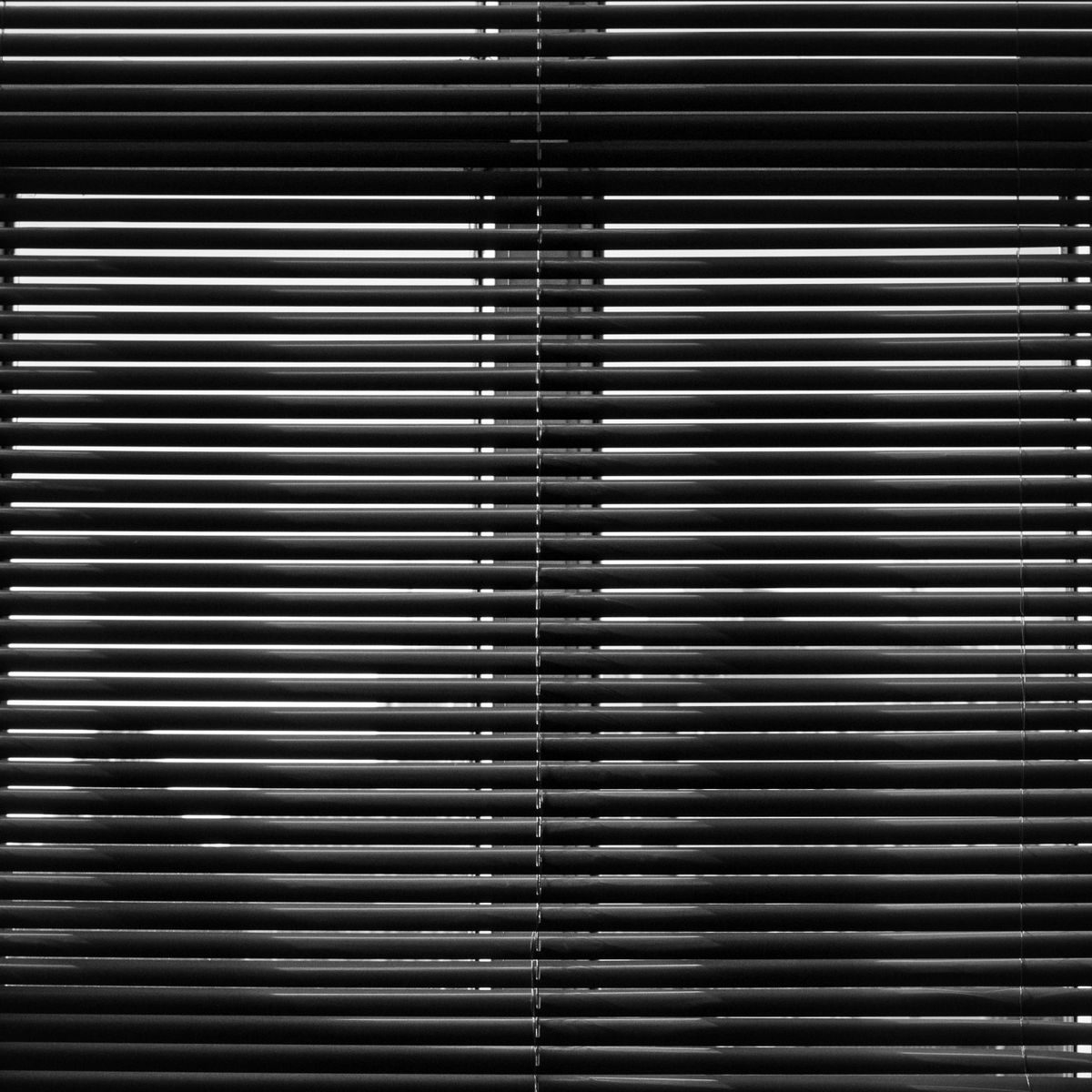 Monochrome close-up of window blinds creating abstract light patterns.