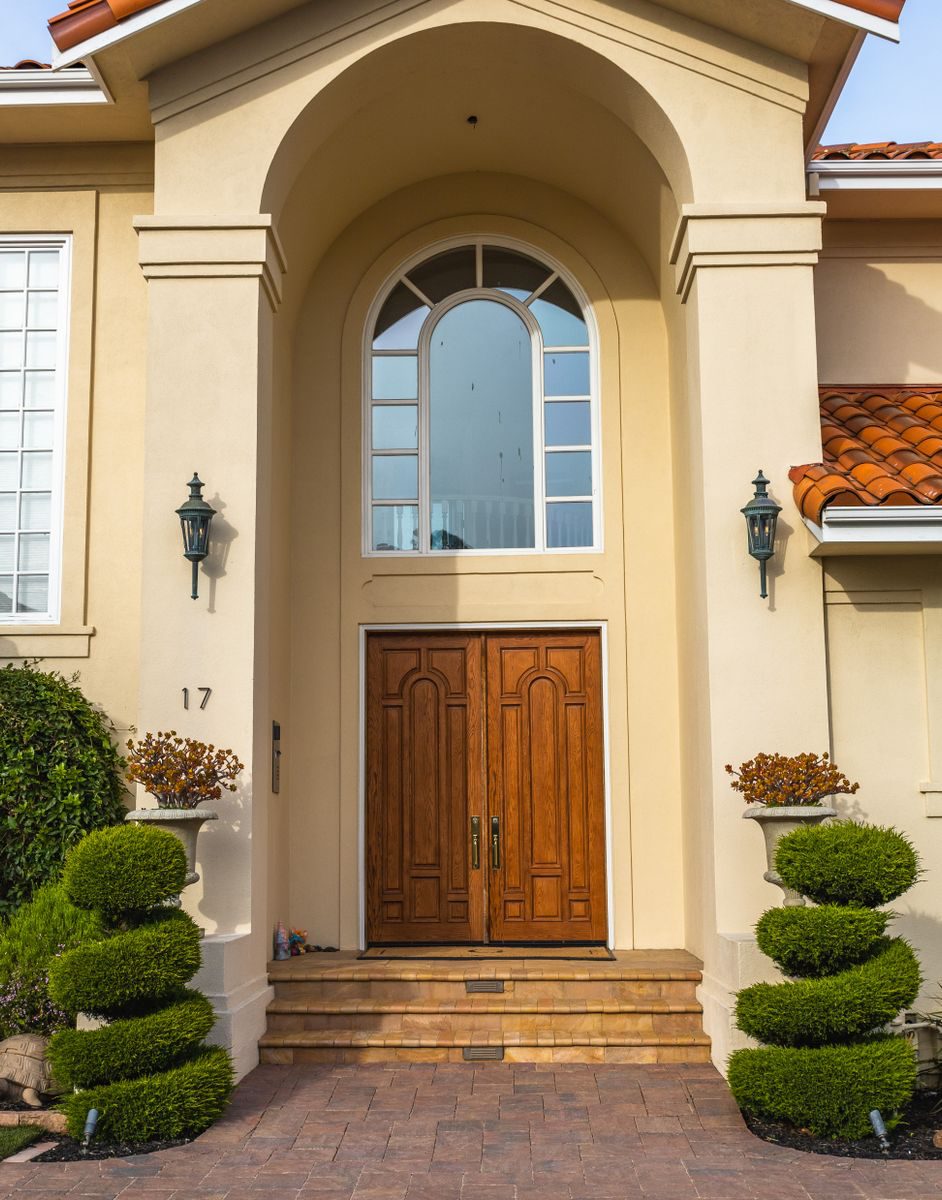Stately entrance featuring double wooden doors and decorative topiary plants.