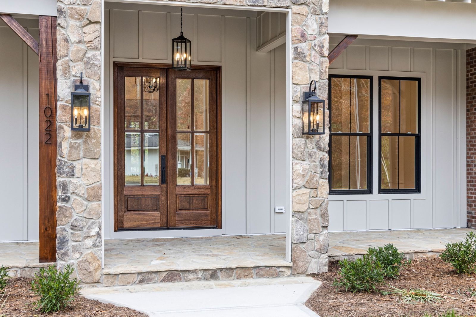 A contemporary stone facade with wooden double doors and lantern-style lighting.