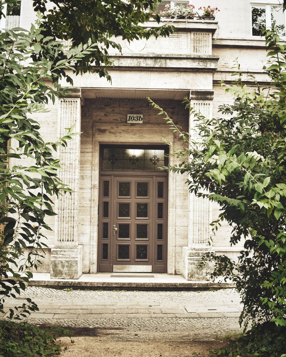 Classic wooden door in Berlin's Karl-Marx-Allee framed by lush greenery.