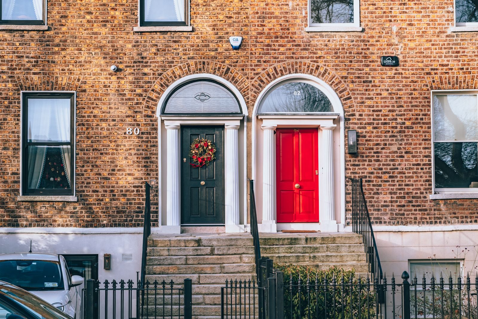A classic brick facade featuring a bold red door and a decorated black door in an urban setting.