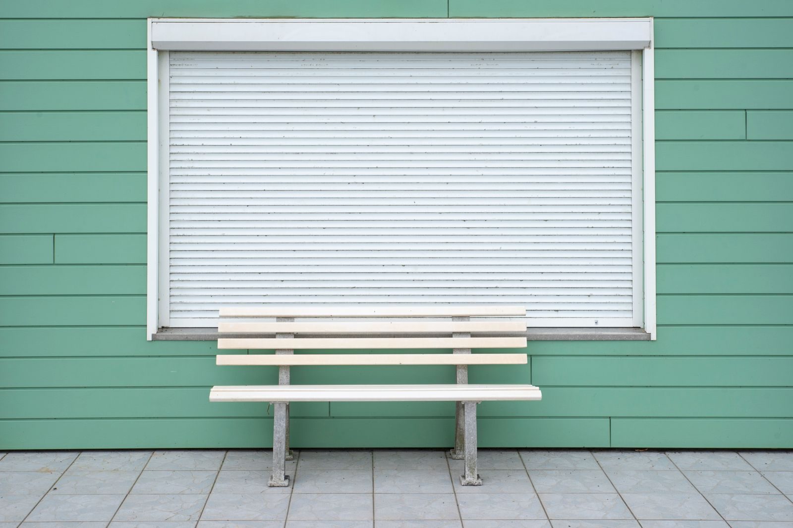 Simple wooden bench by a green wall with closed roller shutter. Ideal for minimalist decor.