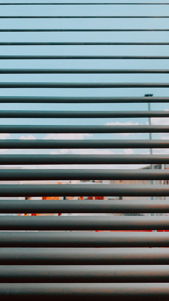 Aesthetic view through window blinds, capturing a cityscape with a warm sky.