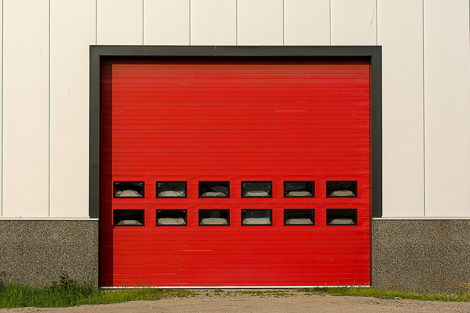 Bright red roller shutter garage door on industrial building exterior.